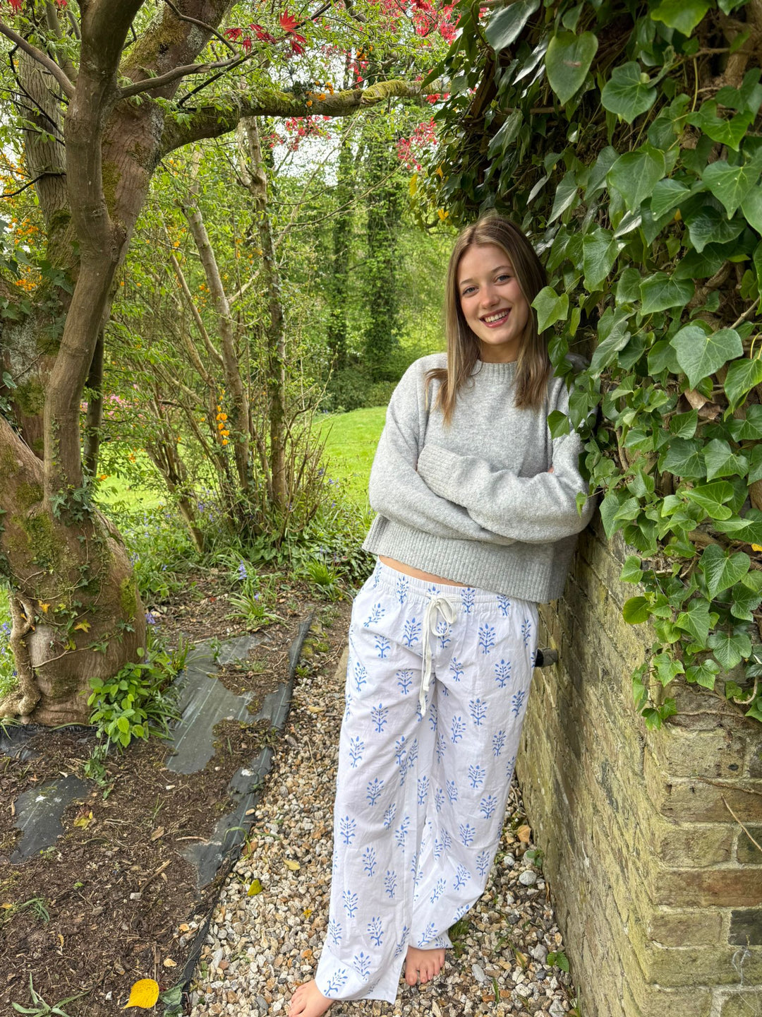 Woman in a garden leaning against a wall with greenery