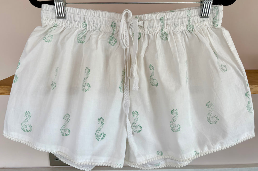 White shorts with green snake patterns on a hanger against a neutral background