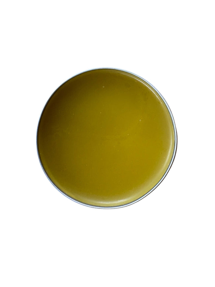 A round metal tin filled with a solid yellow-green balm or wax, photographed from directly above on a plain white background.