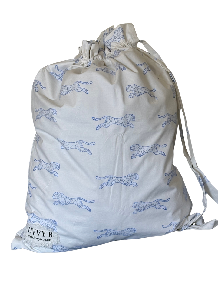 An off-white drawstring storage bag with a repeating blue cheetah print and a small sewn label at the bottom left that reads &