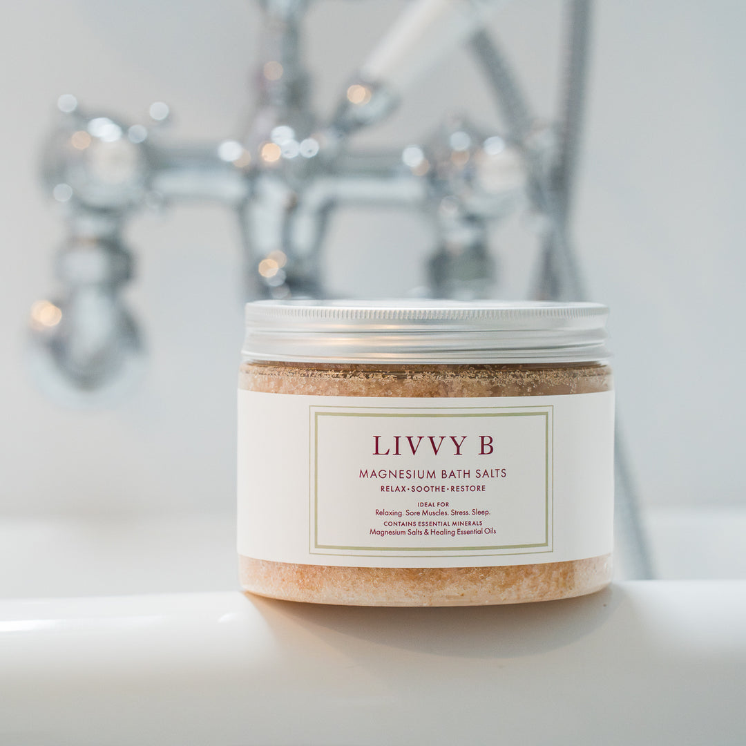 A jar of Livvy B Magnesium Bath Salts on a white surface with a blurred chrome faucet in the background.